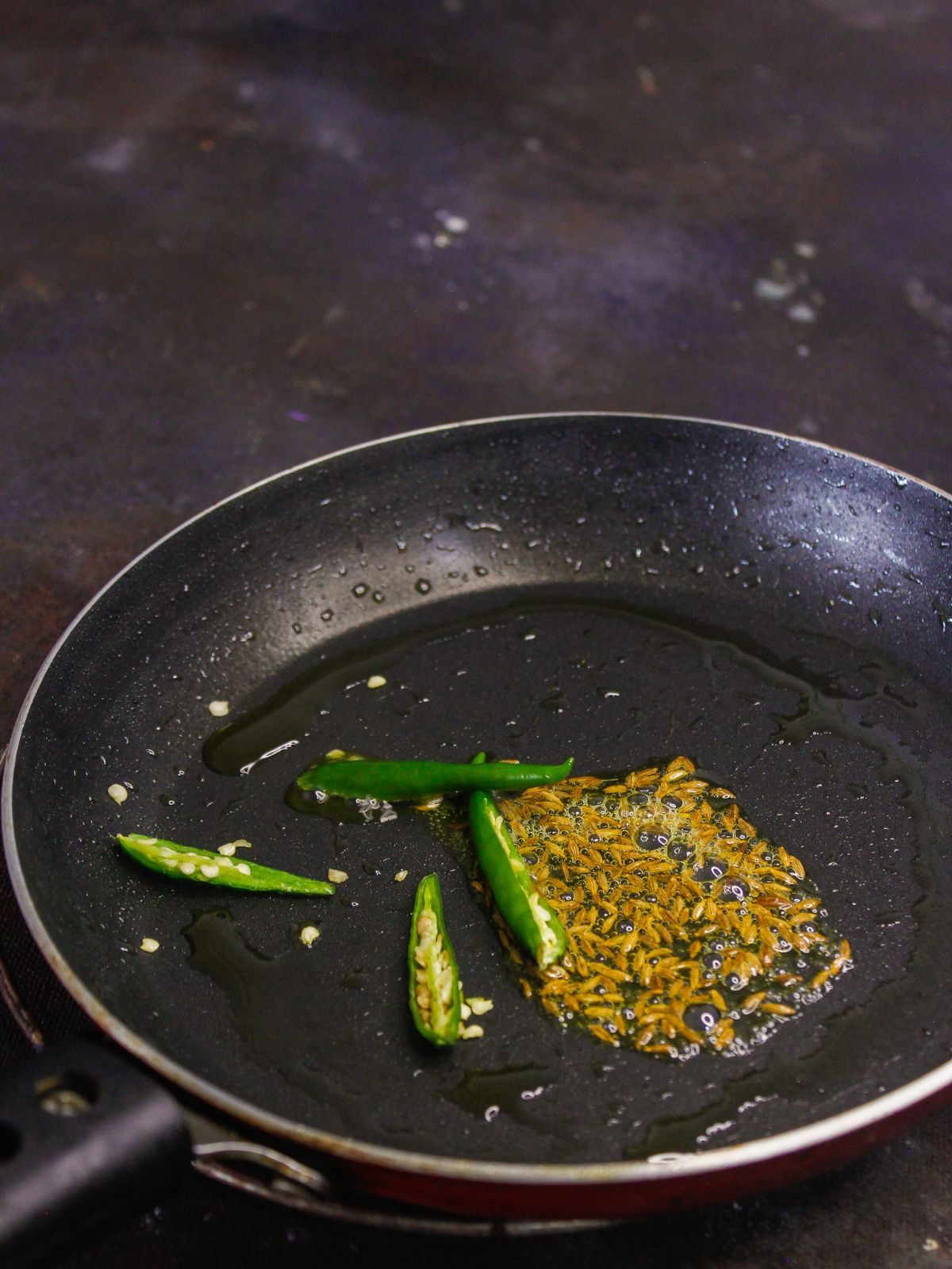 Добавьте семена кумина и зеленые чили в сковороду и обжарьте